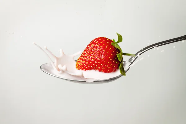 Verse aardbeien spatten in lepel vol van melk — Stockfoto