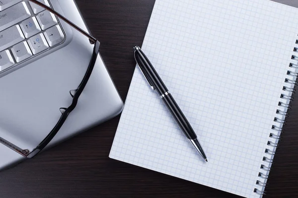 Cuaderno en blanco, bolígrafo, gafas y portátil sobre la mesa — Foto de Stock