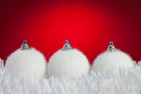 Three white christmas balls on tinsel over bright red background — Zdjęcie stockowe