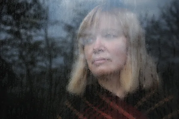 Porträtt av kvinna genom fönstret Stockfoto