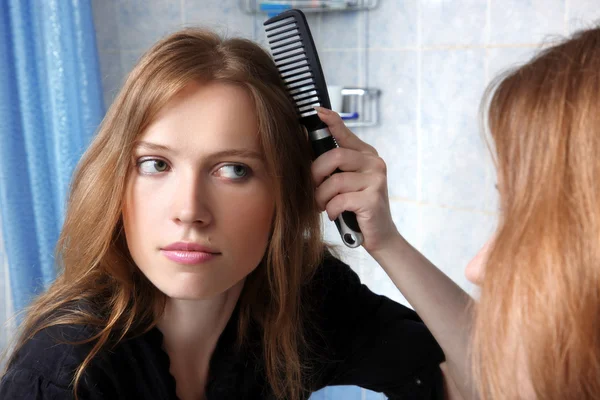 Молодая женщина в ванной перед зеркалом корректирует волосы — стоковое фото