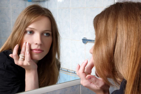 Mujer joven en el baño en frente de un espejo de piel inspeccionada —  Fotos de Stock