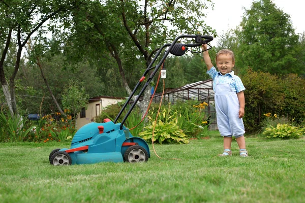 Mały ogrodnik chłopiec koszenia trawnika — Zdjęcie stockowe