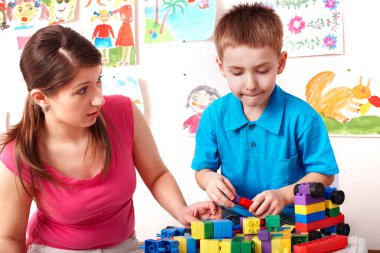 Child with wood block and construction set in play room. clipart