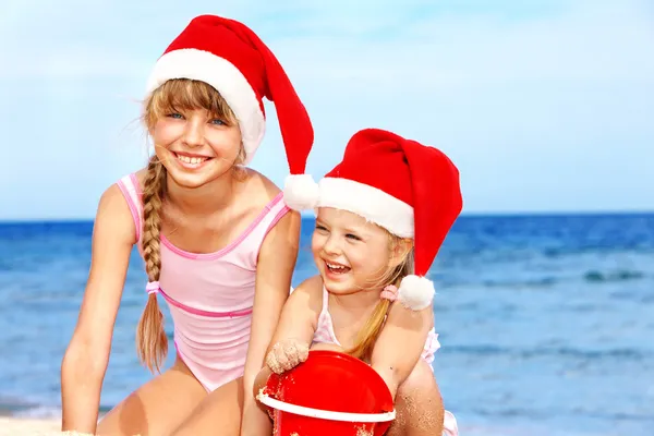 Noel Baba şapkası kumsalda oynarken çocuklarda. — Stok fotoğraf