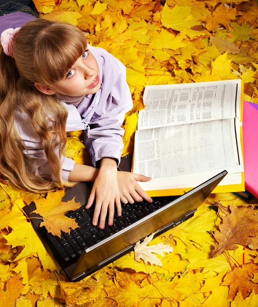 Kid in autumn orange leaves with laptop. — Stockfoto