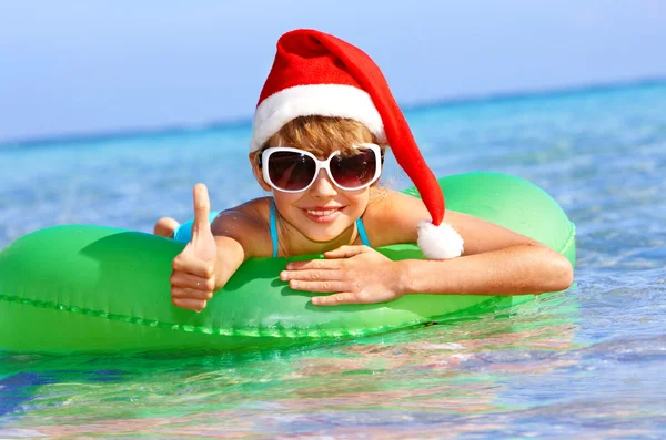 Kind mit Weihnachtsmütze schwimmt auf aufblasbarem Ring im Meer. — Stockfoto