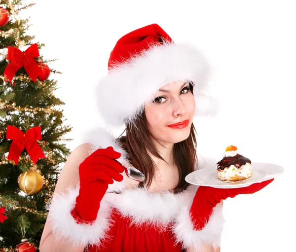 Girl in santa hat eat cake by christmas tree. — Stockfoto