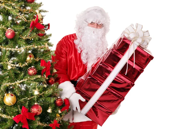 Papai Noel por árvore de natal carregando caixa de presente pilha . — Fotografia de Stock