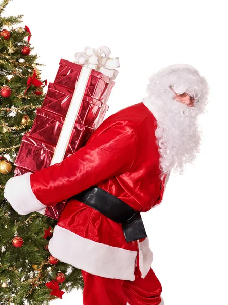 Papai Noel por árvore de natal carregando caixa de presente pilha . — Fotografia de Stock