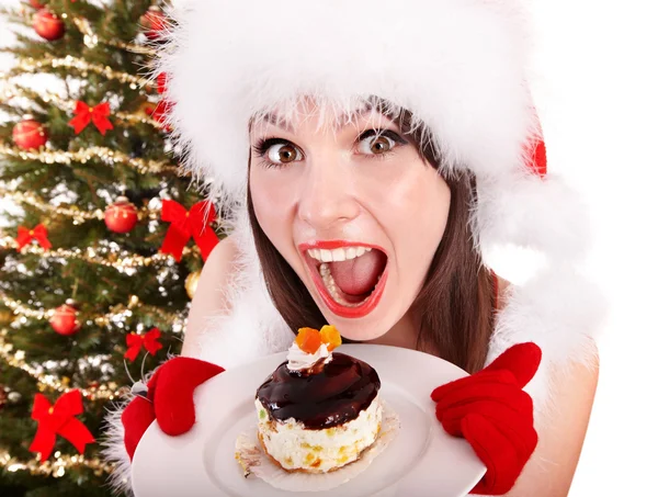 Mädchen mit Weihnachtsmütze essen Kuchen am Weihnachtsbaum. — Stockfoto