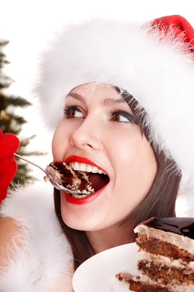 Menina em santa chapéu comer bolo pela árvore de natal . — Fotografia de Stock