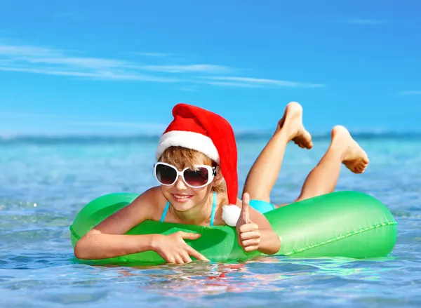 Niño en sombrero de santa flotando en anillo inflable en el mar . — Foto de Stock