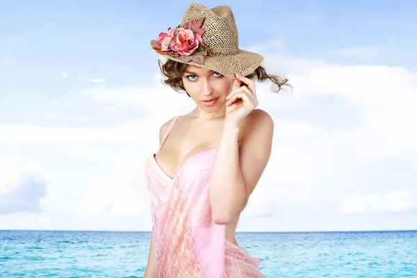 Jonge mooie vrouwen in de roze pareos en hoed in de buurt van zee. — Stockfoto