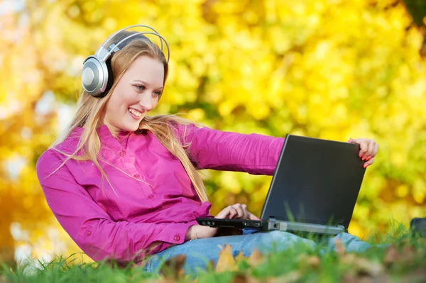 Vrouw met hoofdtelefoon en laptop herfst buitenshuis — Stockfoto