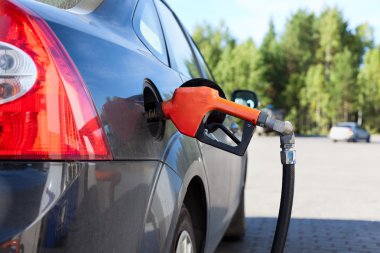 Refueling nozzle in the tank black car at fuel filling column clipart