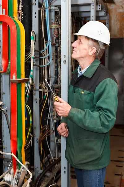 Électricien mature travaillant en casque blanc avec des câbles et des fils — Photo