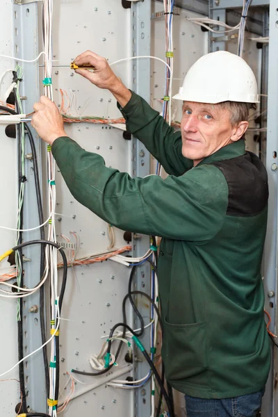 Eletricista maduro trabalhando em chapéu duro branco com cabos e fios — Fotografia de Stock