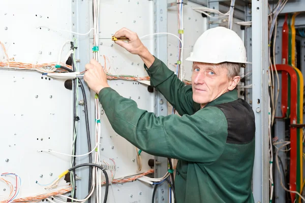 Eletricista maduro trabalhando em chapéu duro branco com cabos e fios — Fotografia de Stock
