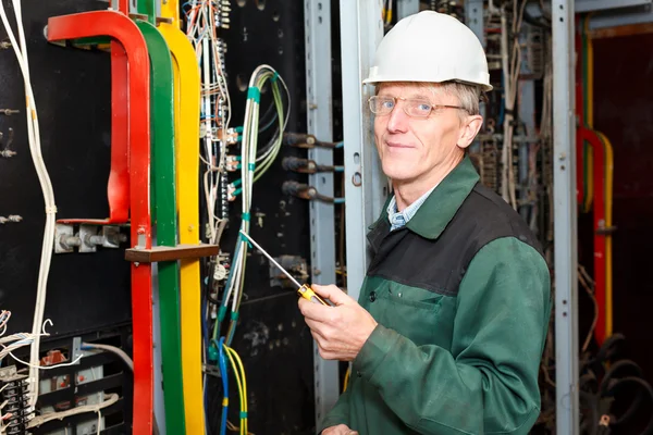 stock image Mature electrician working in white hard hat with cables and wires