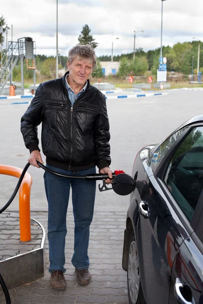 Зрелый мужчина наполняет современный автомобиль бензином на заправках — стоковое фото