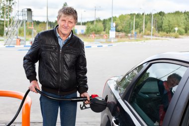 Mature man filling the modern car with gasoline in gas stations clipart