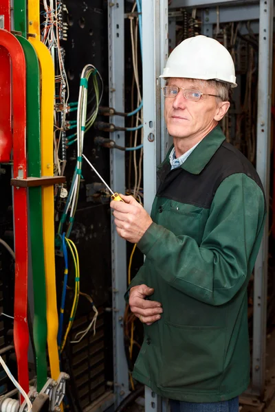 Reifer Elektriker arbeitet in harter Mütze mit Kabeln und Leitungen — Stockfoto