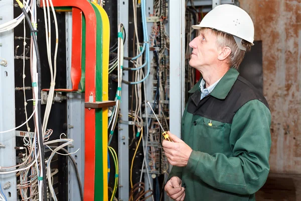 Reifer Elektriker arbeitet in harter Mütze mit Kabeln und Leitungen — Stockfoto