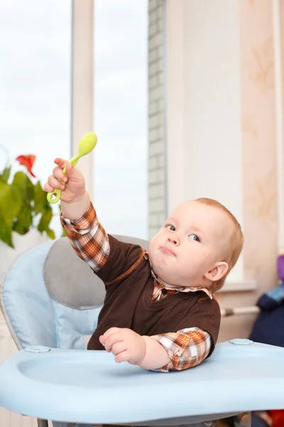 Pequeño niño sentado en la silla alta y agitando su cuchara — Foto de Stock