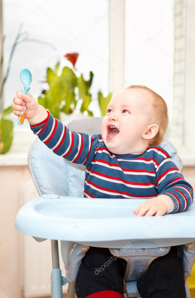 Little kid sitting in highchair and waving his spoon