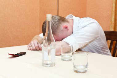 Drunken man laying on table with bottle of vodka clipart