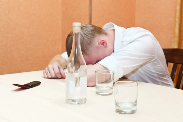 Hombre borracho acostado en la mesa con una botella de vodka — Foto de Stock