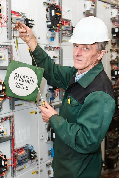 Mature electrician working in white hard hat with caution board — Stock Photo, Image