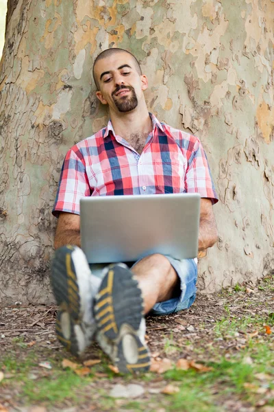 Młody człowiek z komputerem w parku — Zdjęcie stockowe