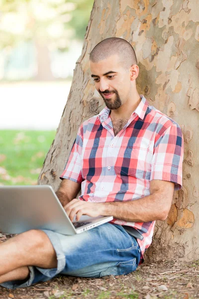 Νεαρός άνδρας με υπολογιστή στο πάρκο — Φωτογραφία Αρχείου