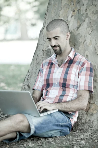 Mladý muž s počítačem v parku — Stock fotografie