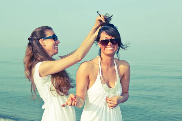 Jovem mulher vestir os cabelos de seu amigo no litoral — Fotografia de Stock