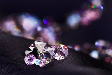 Diamond (small purple jewel) stones heap over black silk cloth b clipart
