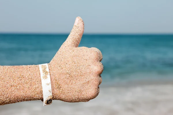 Hand gesturing thumb up on sea beach — Stock Photo, Image