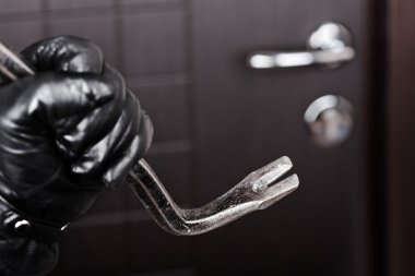Burglar hand holding crowbar break opening door clipart