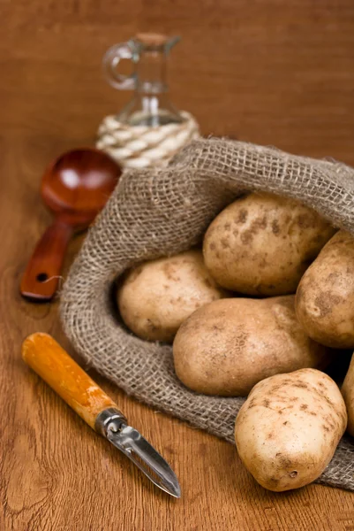 Patatas en saco de arpillera con un cuchillo rústico para limpiar el vegetab — Foto de Stock
