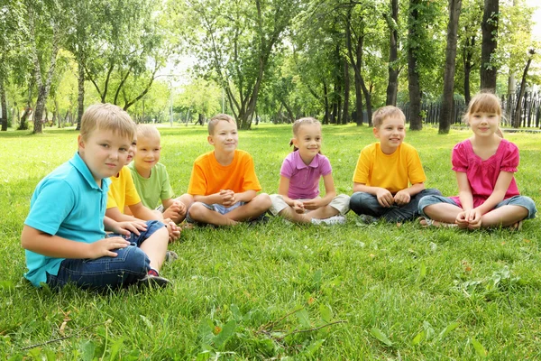 Grupa dzieci siedzi razem w parku — Zdjęcie stockowe