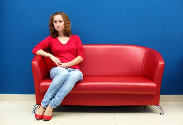 Jovem mulher sentada no sofá vermelho — Fotografia de Stock