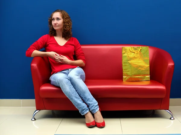 Giovane donna seduta sul divano rosso — Foto Stock