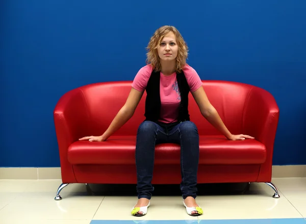 Молодая женщина сидит на красном диване — стоковое фото