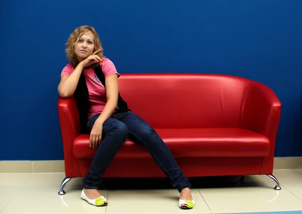 Jeune femme assise sur un canapé rouge — Photo