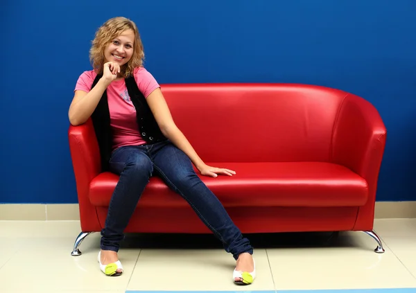 Jonge vrouw zittend op rode sofa — Stockfoto