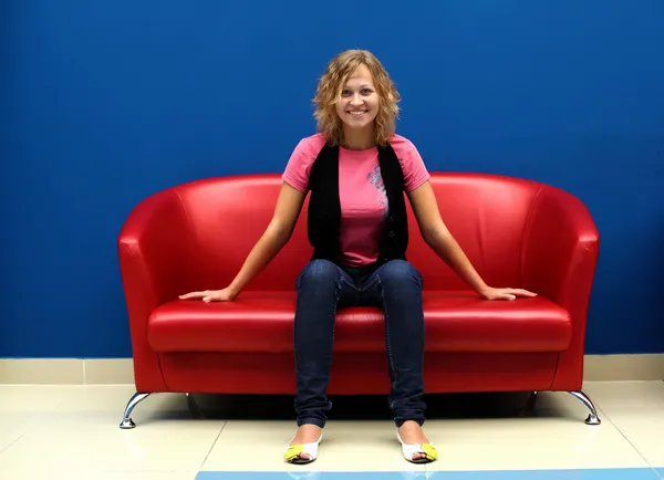 Mujer joven sentada en un sofá rojo — Foto de Stock
