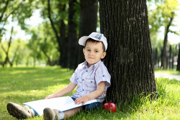 Retrato de um menino com um livro no parque — Fotografia de Stock