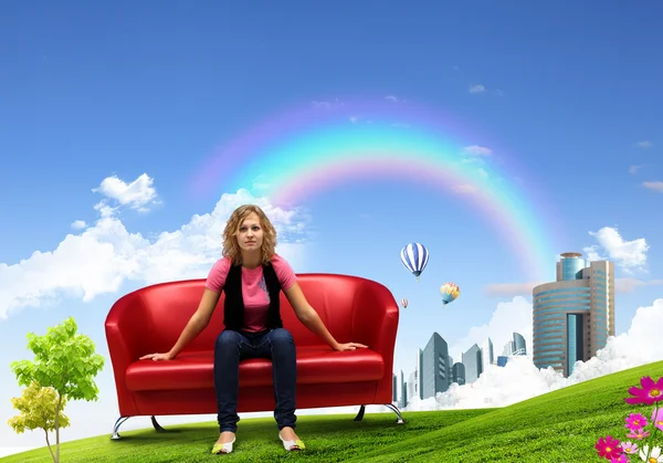 Ung kvinna sitter på soffan natur bakgrund — Stockfoto